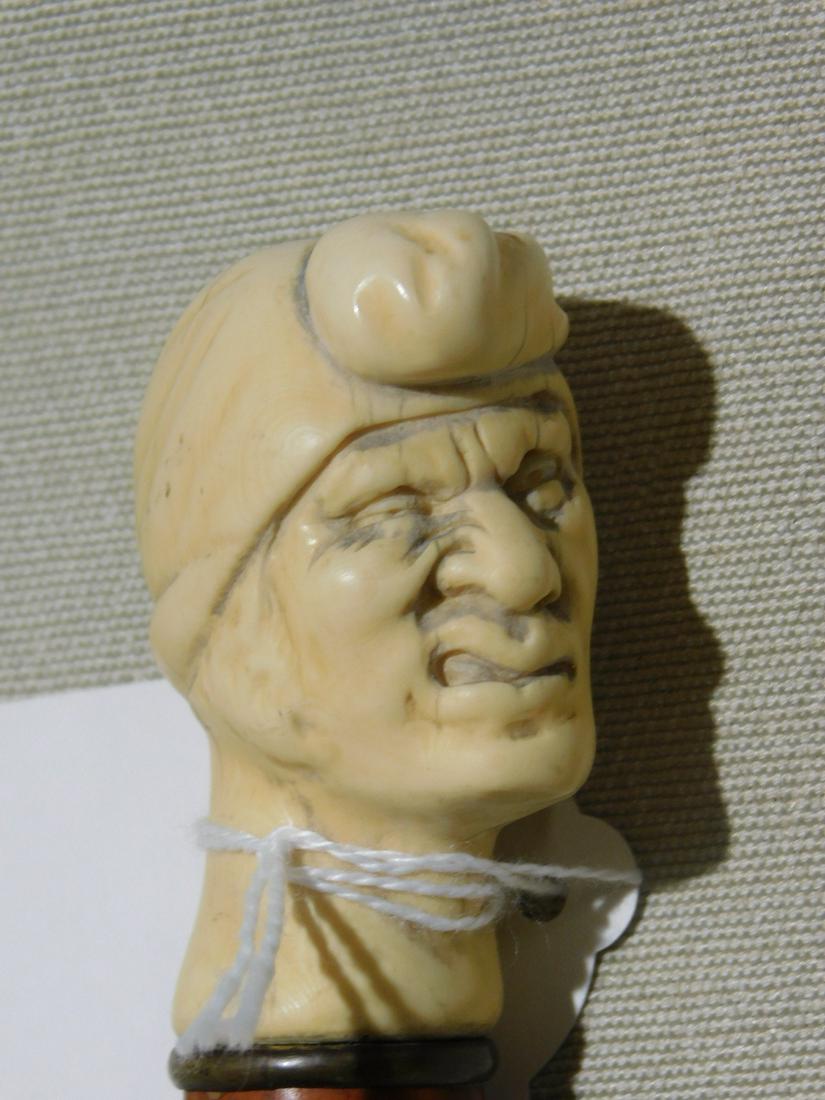 Grotesque Head Cane: Grotesque Head Cane. Handle: Carved bust of grotesque man wearing a turban. Collar: brass ring. Shaft: Brown lacquered finish wood. Ferrule: Brass and iron.. Length: 36". Vintage: 19th / 20th C. [38] 