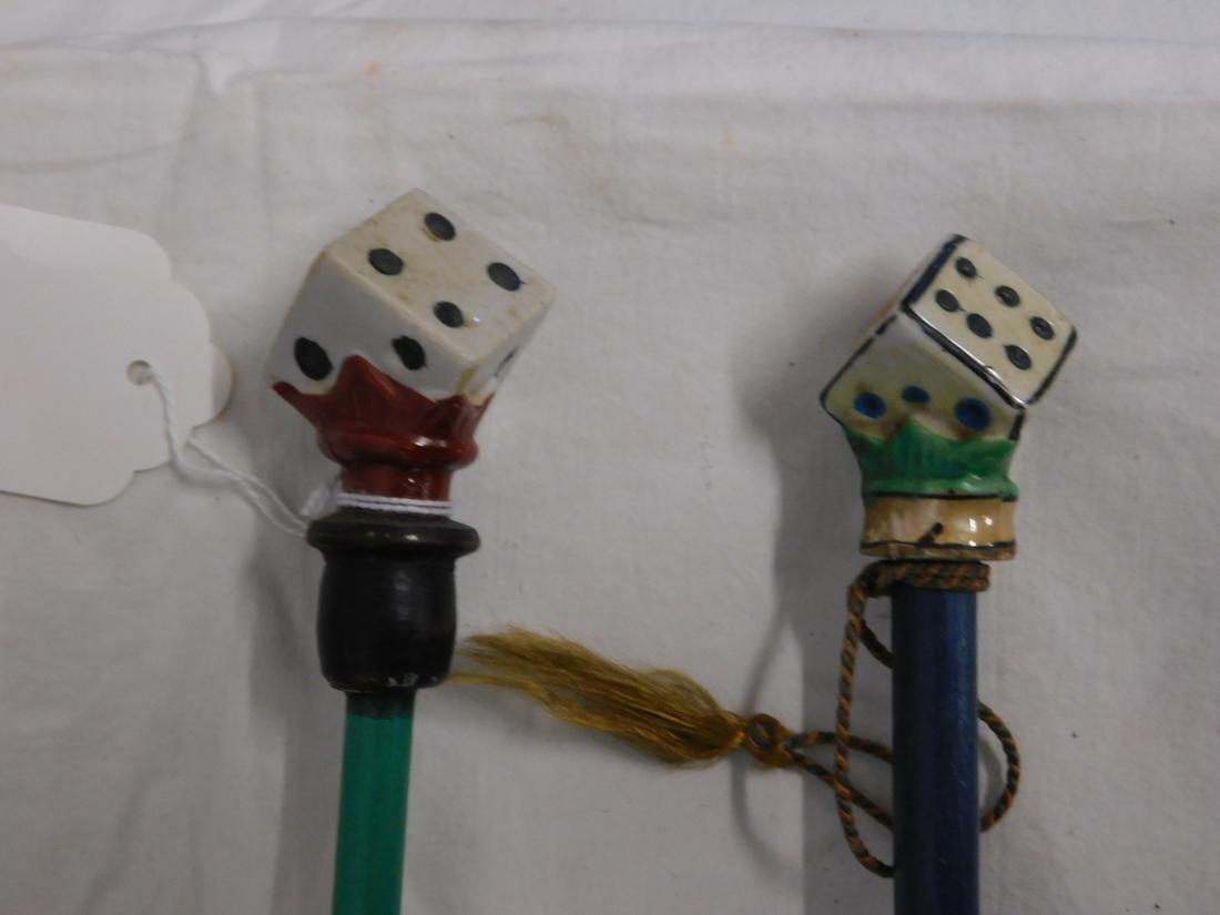 2 Dice Carnival Canes: Two Dice Carnival Canes, porcelain painted dice handles, one with a black wood collar, green and blue wood dowel shafts, one with metal ferrule, lengths 33 1/2: and 35". [87] CONDITION: Very good, lig