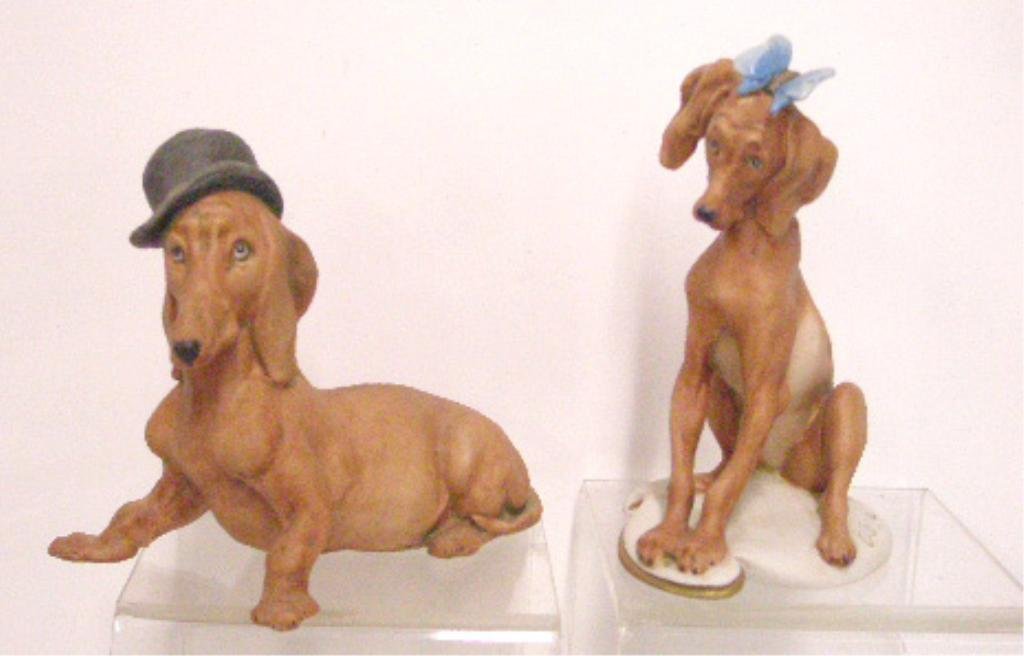 Giuseppe Cappe Porcelain Dog Figurines: Lot of two Giuseppe Cappe Italian porcelain dog figurines, 4" x 4 3/4" reclining Dachshund with Bowler hat & 5" x 3 1/4" seated Dachshund with butterfly in hair. [270] CONDITION: Very good with no dam