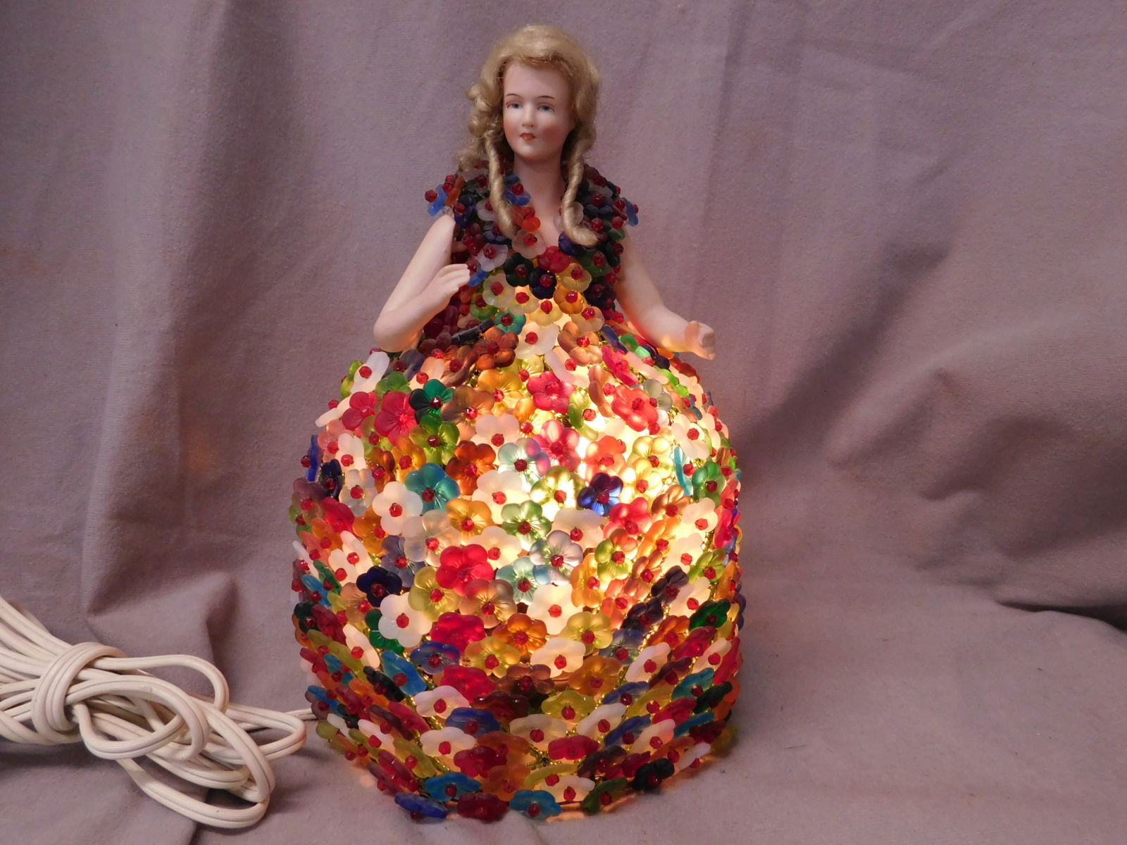 German Half Doll Lamp: German Half Doll Lamp, painted porcelain half girl body with jointed out stretched arms; long yellow wig; glass multi colored flower forms create her dress upon a metal inner frame with electric light