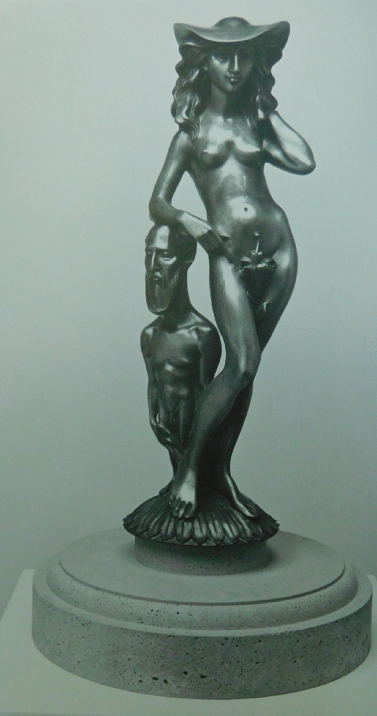 Stephen Robin Bronze Female Sculpture w/ Artist: Stephen Robin (1944 - 2018) bronze casting, female sculpture with artist, semi nude female with hat, leaning on (smaller) artists head, 18 3/4" h. on attached 12" diam. stepped base, upon a white wood