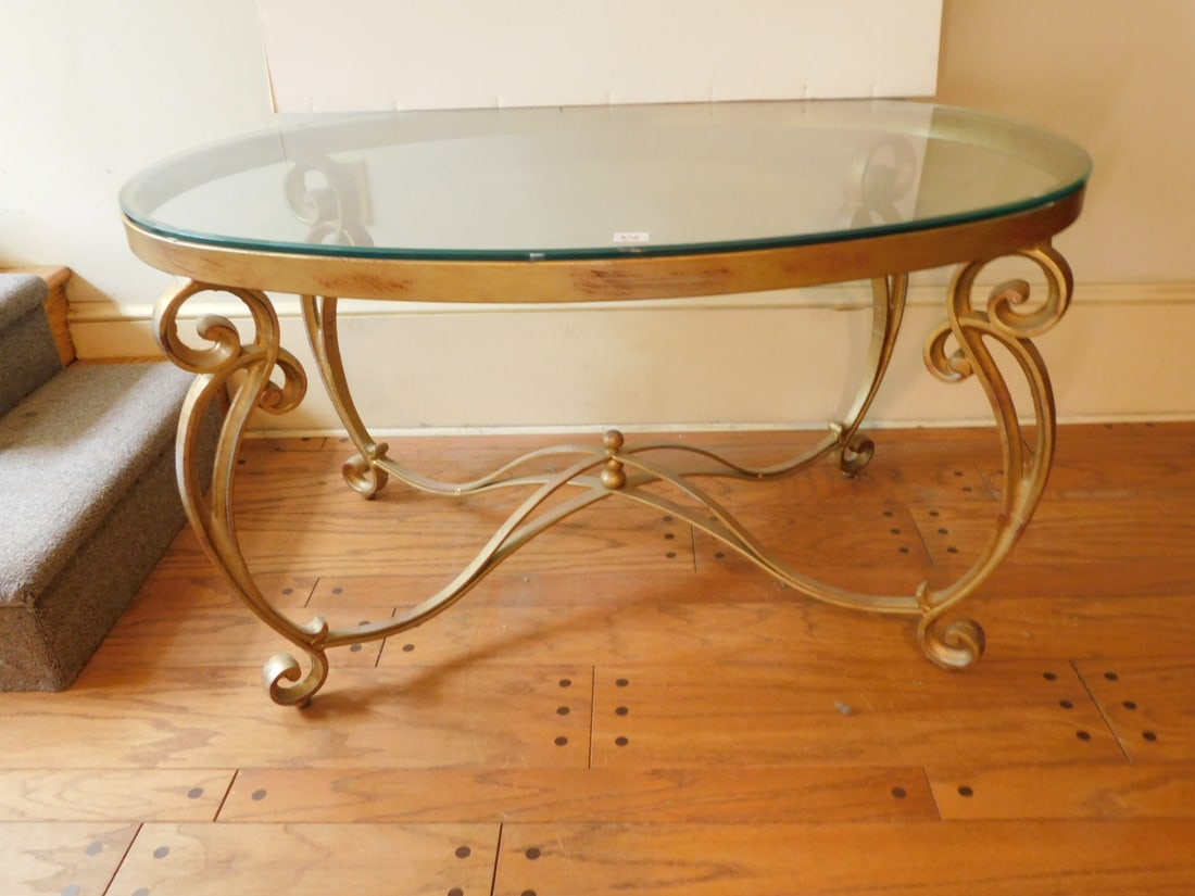 Glass and metal coffee table: Glass and metal coffee table, oval, beveled glass top, gold painted floral scroll legs with stretcher, 44" x 30" x 24" h. Condition: glass needs cleaning