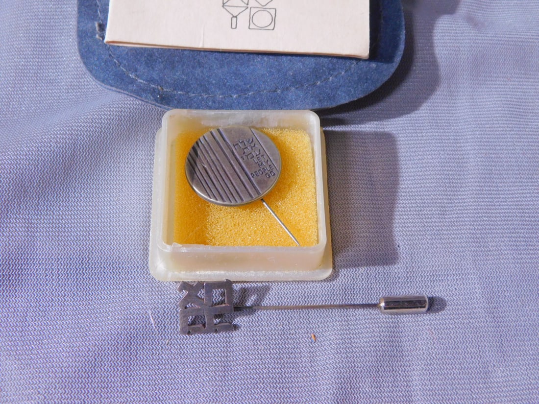 2 Israeli Silver Stick Pins: Two Israeli Silver Stick Pins, includes: Robert Indiana Ahava (Love) stick pin; original certificate of authenticity; and a Bank of Israel; dish form pin inscribed in Hebrew and English "Let My People