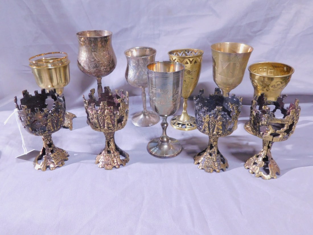 11 Kiddush Goblets: Eleven Kiddush Goblets, includes: four Brutalist heavy brass Temple scene 4 1/2" goblets missing glass liners, plus seven assorted silver plate and brass goblets from 5" to 6 3/4". [86] CONDITION: Bru