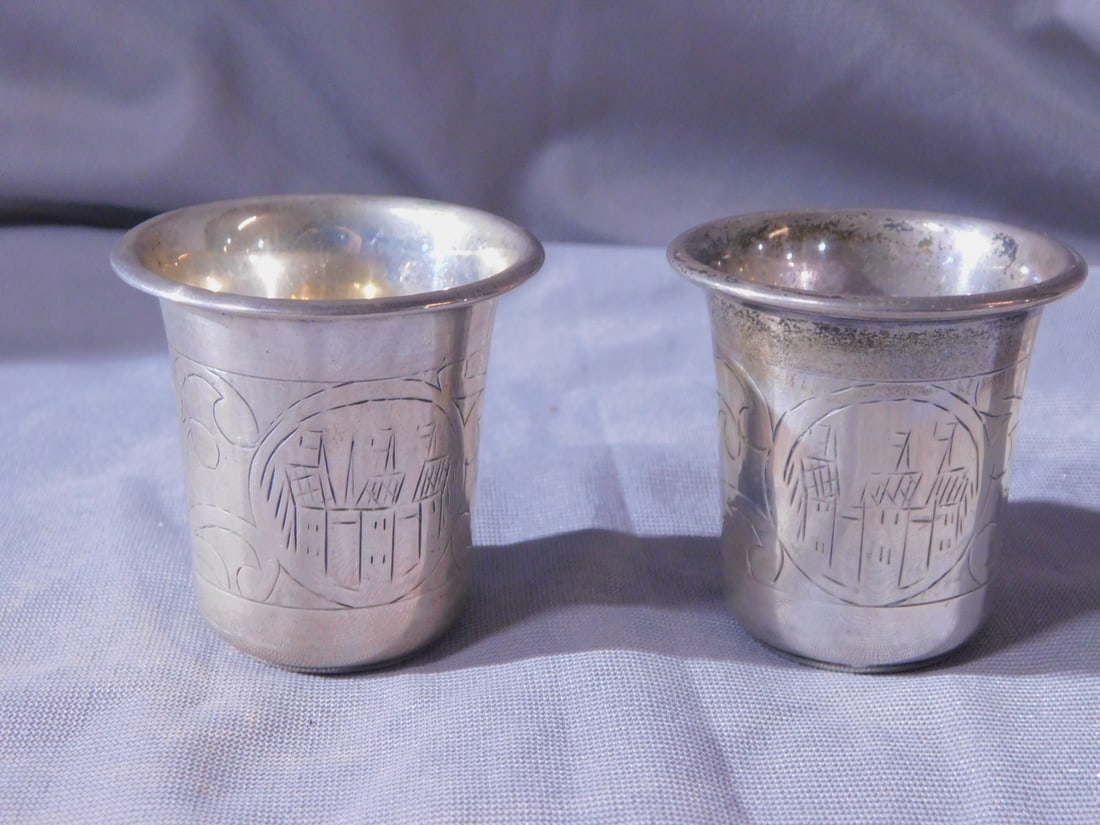 2 Russian Kiddush Cups: Two Russian Kiddush Cups, 84 silver purity and other touch marks, village scenes and scroll etchings, late 19th C, 2"h, 2.55 ozts TW. [103] CONDITION: Very fine.