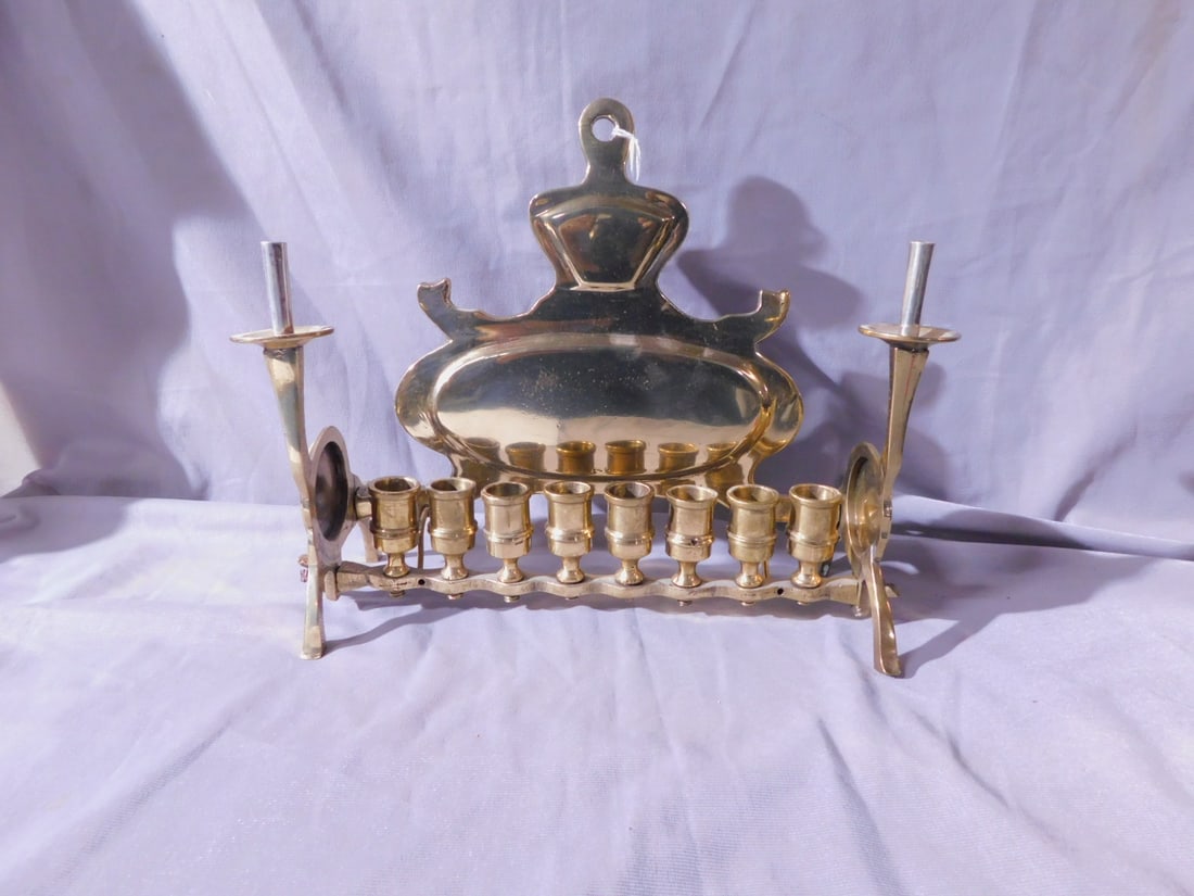 Brass Menorah: Brass Menorah, groomed oval back, a bar with eight urn form candleholders is supported on each end by tall candleholders with disk bodies and attached with wing nuts, early 20th c, 11" x 9" x 4". [61]