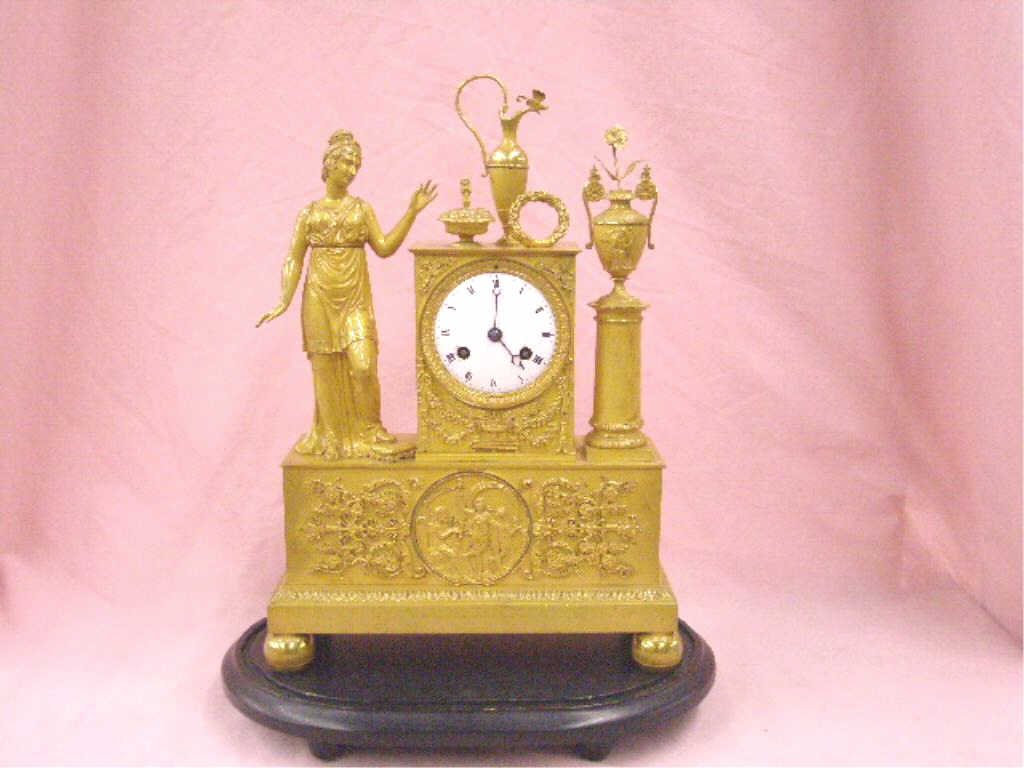French Empire Figural Bronze Mantle Clock: 19th c. French Empire style gilt bronze 14 1/4" x 10" x 3 1/2" figural mantle clock, modeled as a Roman or Greek style maiden with foot on stool on one side, complemented by a floral urn on column sta