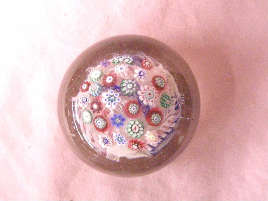 Antique Millefiori Glass Paperweight: Antique unsigned clear glass 2" x 2 1/2" paperweight with multi color Millefiori cane and ribbon design. CONDITION: Wear and scratches on base and surface. One cane has a raised inclusion inside. See 