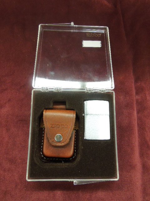 Zippo Lighter: Zippo lighter (brushed chrome) with brown leather carrying pouch, new in plastic fitted case with cardboard outer cover. CONDITION: New old stock.