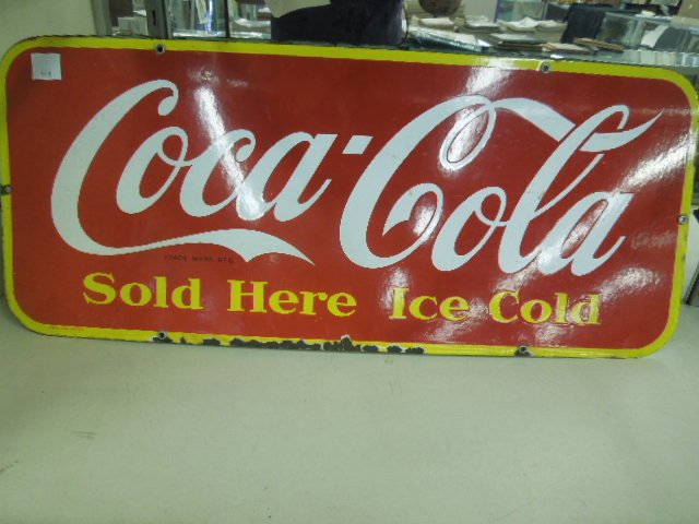 Mid 20th c. Porcelain Coca-Cola Advertising Sign: Mid 20th c. porcelain Coca-Cola advertising sign, "Sold Here Ice Cold", 12" x 29". CONDITION: Enamel off on bottom wear throughout, one hole (left) ring gone.