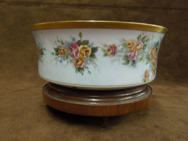KPM Kirster German Center Bowl: KPM Krister Germany Center bowl, on wood stand, over roses & putti transfer print decorations, D 8 3/16" bowl hgt 3 1/4", mid 20th c. [6] CONDITION: Modest wear.