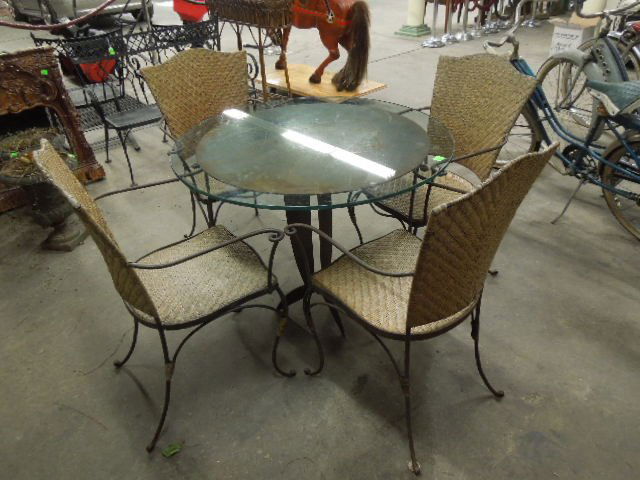 5 Pc Patio Set, Cut Steel & Glass: Five piece patio set, cut steel & glass table & four wrought iron & caned chairs, table 29 1/2" diameter, 35 1/2" height. CONDITION: Wear & some rust to table & to table 7 chairs, some wear to rush es