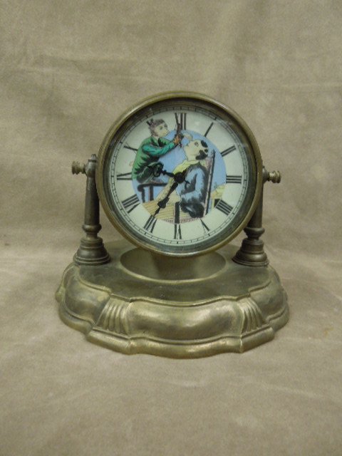 Swivel Animated Desk Clock: Brass swivel desk clock, hand painted face (sheep shaving man) animated arm with razor, wind up, early 20th C., 4 1/2" d clock on 7 1/2" molded brass base. CONDITION: Minor wear especially around scre