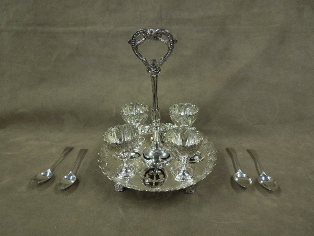 S.P. Soft Boiled Egg Stand w/Sterling Spoons: Silver plate soft boiled egg stand, 7" diam x 8 1/2" h with four footed cups, 2 1/2" h raised floral design around rim on fitted (with pegs) footed stand, open heart from long handle, marked (FGE & Co