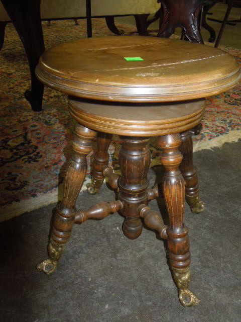Piano Stool Honey Finished Hardwood: Piano stool, honey finished hard wood, adjustable rotating seat, brass claw around glass ball feet, early 20th C. CONDITION: Areas of finish loss.
