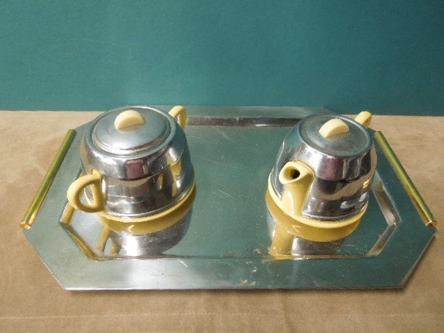 Art Deco Chrome & Ceramic Tea Set: Art Deco chrome & ceramic tea set, four pieces, yellow ceramic bodies marked "Made in England" with chrome covers & lids with yellow Bakelite finials; includes: teapot, covered sugar, covered creamer,