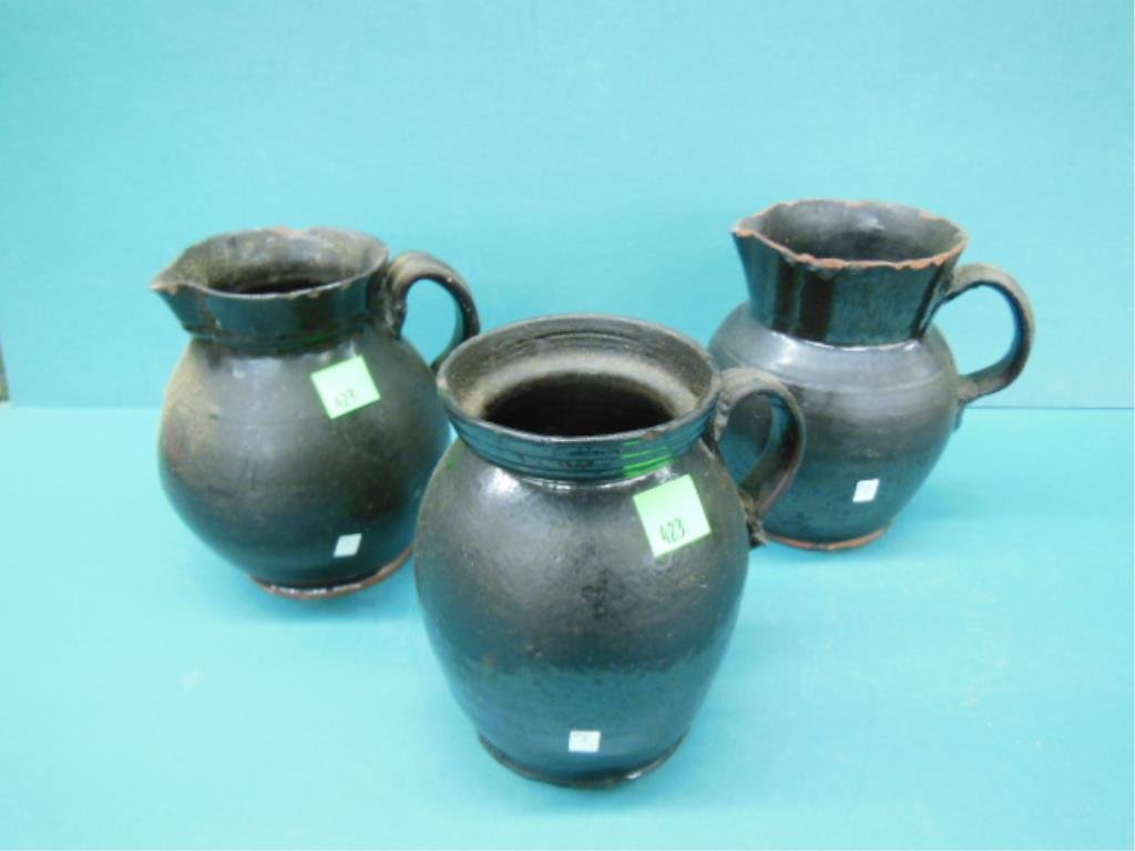 Three 19th c. Redware Pitchers: Three 19th c. Redware pitchers, with handles, having a dark brown glaze, all from digs in Phila, PA, approx hgt 8". CONDITION: All with numerous chips 2 with repaired handles.