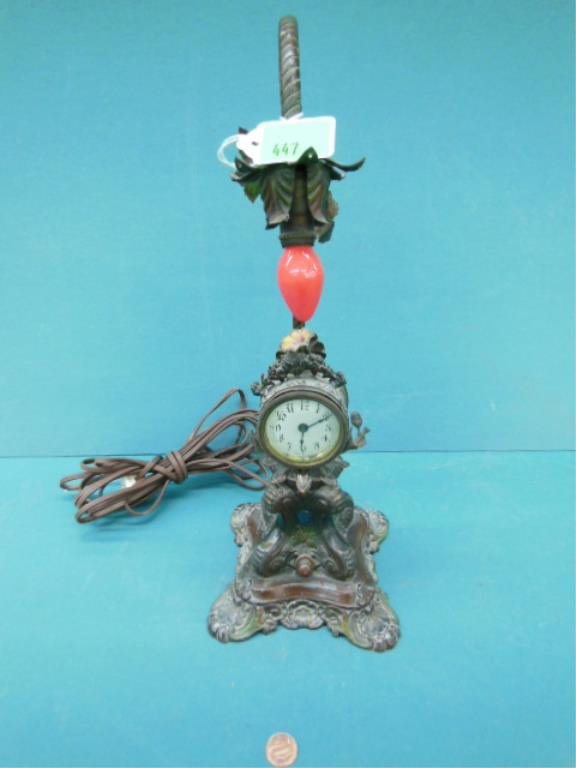 Clock/Lamp: Clock/Lamp, bronzed spelter metal, floral crest clock on urn base hovered over by a pendant light, wind up movement, early 20th c. H 15". CONDITION: Clock not running and does not fit tight into frame