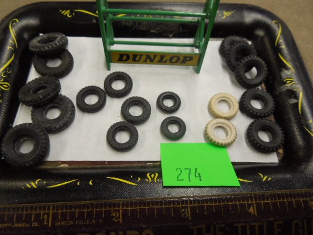 18 Dinky Toy tires & Dunlap Stand: Eighteen Dinky toy tires & Dunlap stand, five 7/8"d, five 11/16" d, six 9/16"d (two white) & two 1/2"d, plus green metal "Dunlap" tire stand 2 1/8" x 2"h, mid century. CONDITION: Minor wear from age.
