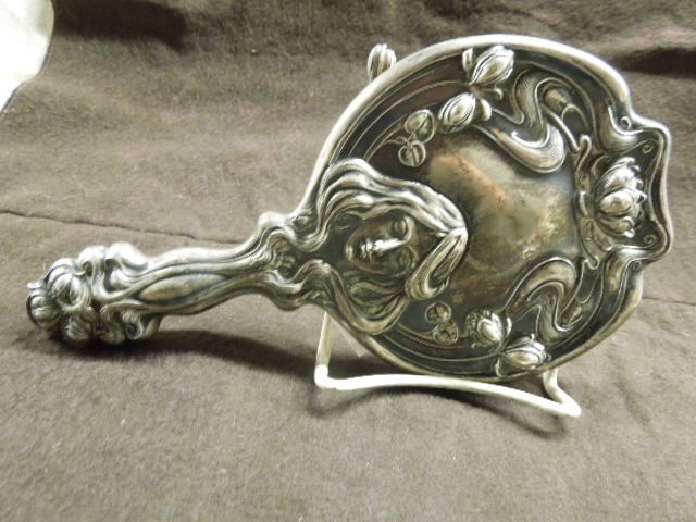 Art Nouveau Dressing Mirror: Art Nouveau dressing mirror, Repousse design of woman w/flowing hair & flowers. Hallmark of Shield & letters S & D, 9 1/2" (length) x 5" (width). CONDITION: Minor scratches on mirror.