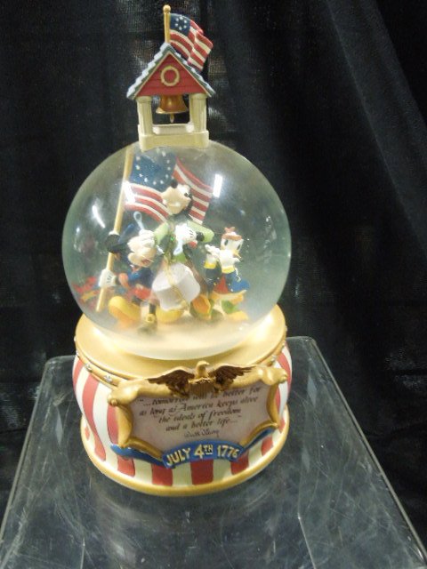 Disney 4th of July Musical Snowglobe: Disney 4th of July musical snowglobe featuring: Mickey, Goofy and Donald as the flag carrier, drum and fife (in globe) with white and red stripes on base, eagle plaque "...Tomorrow Will Be Better, For