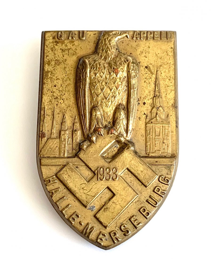 1933 GERMAN WWII GAU HALLE-MERSEBURG TINNIE BADGE: Original era manufacture. Attractive gilded brass shield-shaped tinnie with a pinback reverse. Measures 23x50mm. Very clean.