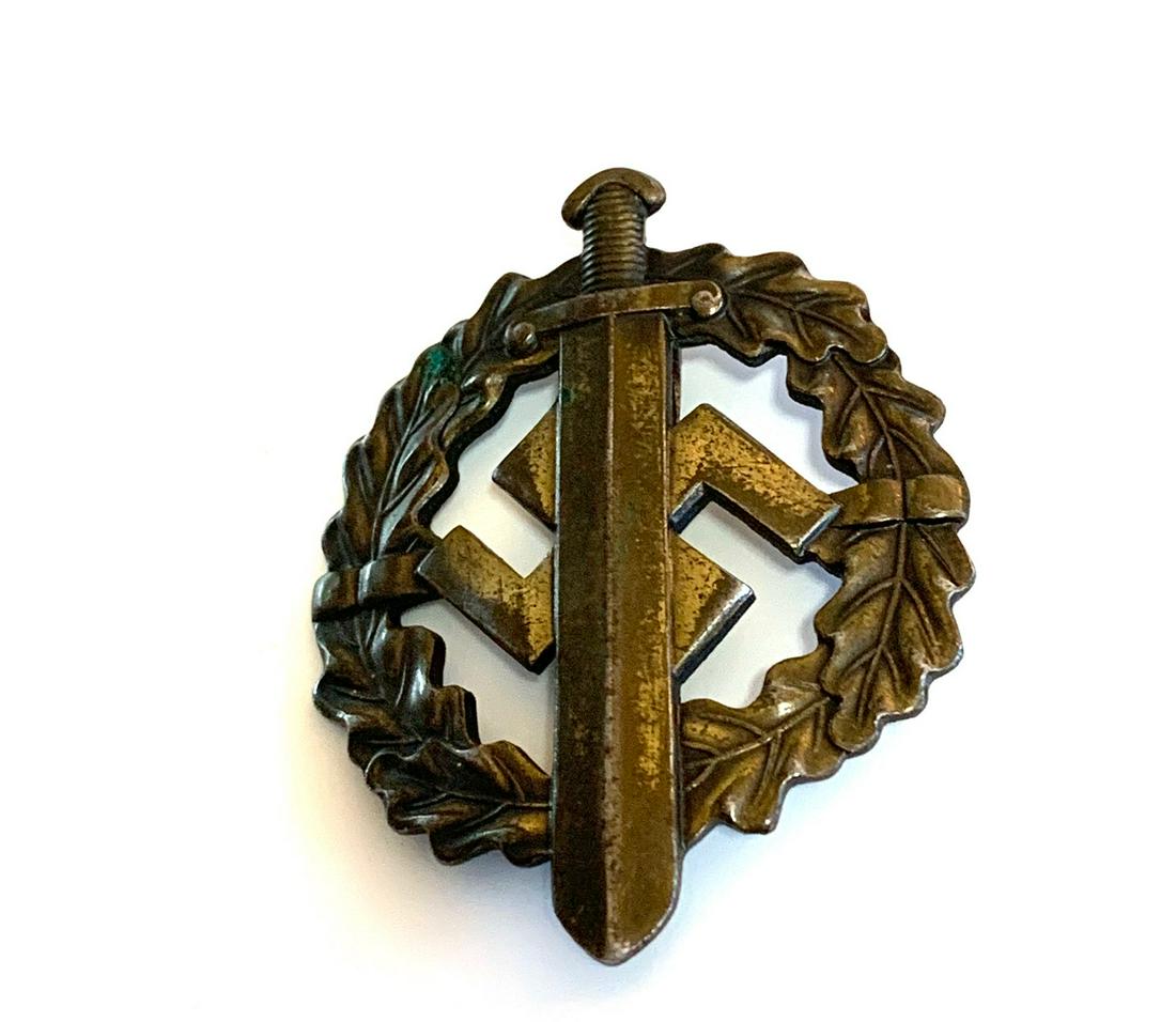 WWII GERMANY SA. A SA SPORTS BADGE BRONZE GRADE: (SA Sportabzeichen in Bronze). The obverse consisting of a circular oak leaf wreath, overlaid by a sword and mobile swastika, vertical pinback, marked â€œFECHLER, BERNSBACH/SA”,