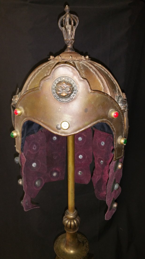 Warrior battle Helm- Theatrical Vintage: A decorative helmet of brass and sheet metal fabrication with merlot red suede neck guard fringe, metal grotesque face appliques , red and green inset glass beads. Lined in black fabric. A center ston