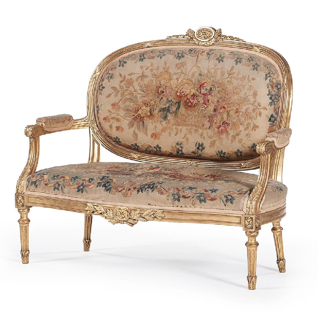 Louis XVI-style Needlepoint Canapé: French, 19th century. A needlepoint canapé in giltwood, having an oval back surmounted by a floral crest, padded seat and arms, and conforming carved and reeded apron, raised on circular fluted leg