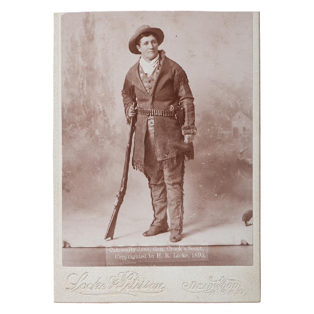 Calamity Jane Cabinet Photograph by H.R. Locke: Cabinet card showing Calamity Jane armed with a repeating rifle, ammunition belt, and revolver, with imprint of Locke and Peterson, Deadwood, SD, titled in the negative "Calamity Jane, Gen Crook's Sco