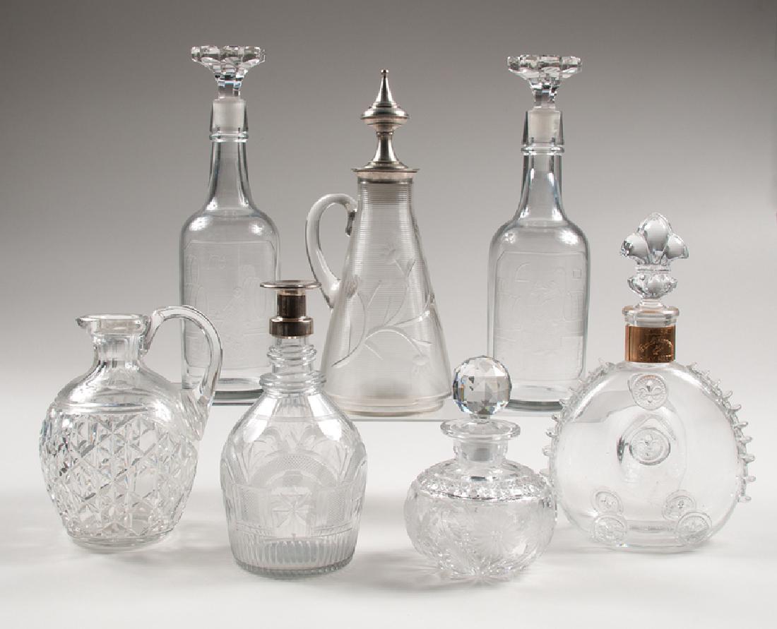Glass Liquor Decanters: 20th century. A group of seven glass liquor decanters, including:Â one Louis XIII Cognac Baccarat bottle with original stopper;Â two intaglio glass decanters with scenes in a wine cellar, each m
