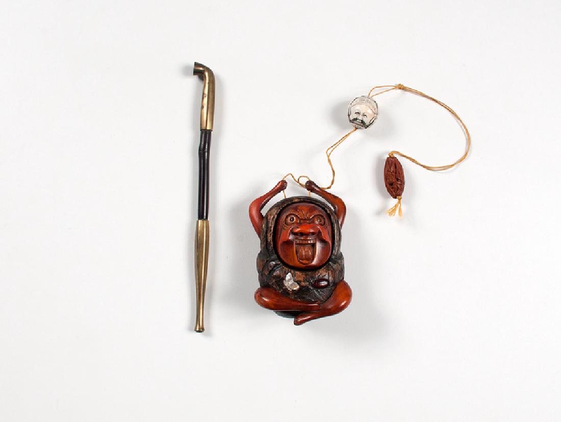 Japanese Daruma Tonkotsu with Kiseru: Japanese. A carved tonkotsu tobacco box in the form of Daruma with inlaid mother of pearl butterfly and hardstone beetle, suspended from a string with an ivory ojime and carved wood bead; included is 