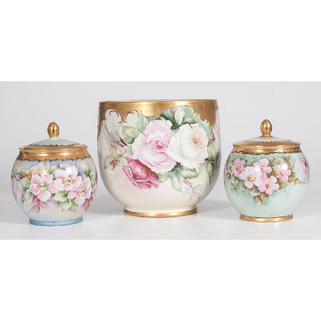 Limoges Porcelain Cache Pot and Lidded Jars: French. A group of porcelain vessels including a cache-pot and two lidded jars, all decorated with floral designs, each signed by three different artists, including Eleanor Gordon Weston, Riley, and B