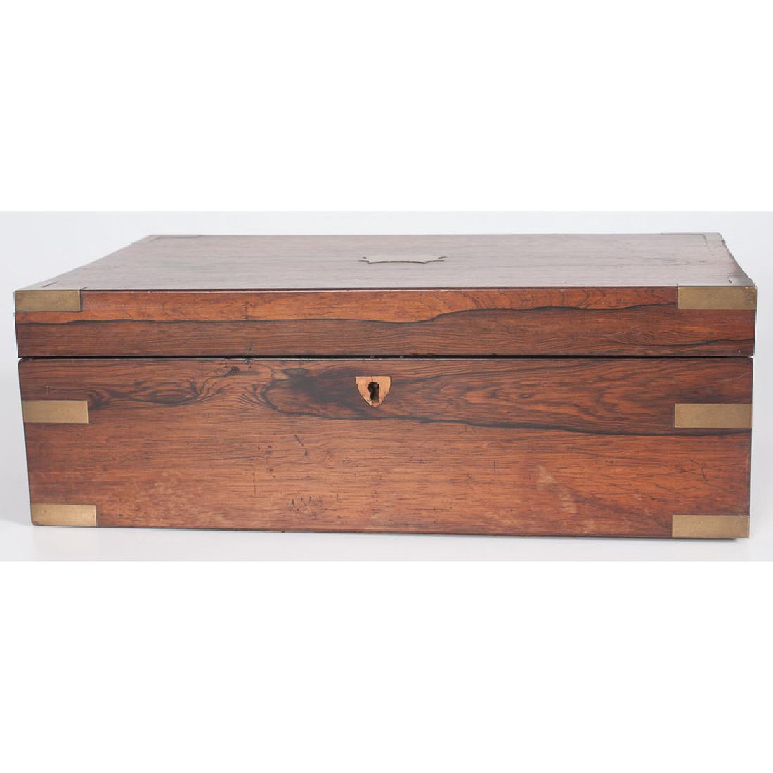 English Lap Desk with Brass Mounts: English, late 19th century. A lap desk with brass mounts, the top opening to a red velvet sloped writing surface covering two storage compartments, a covered pen tray and three small storage compartm