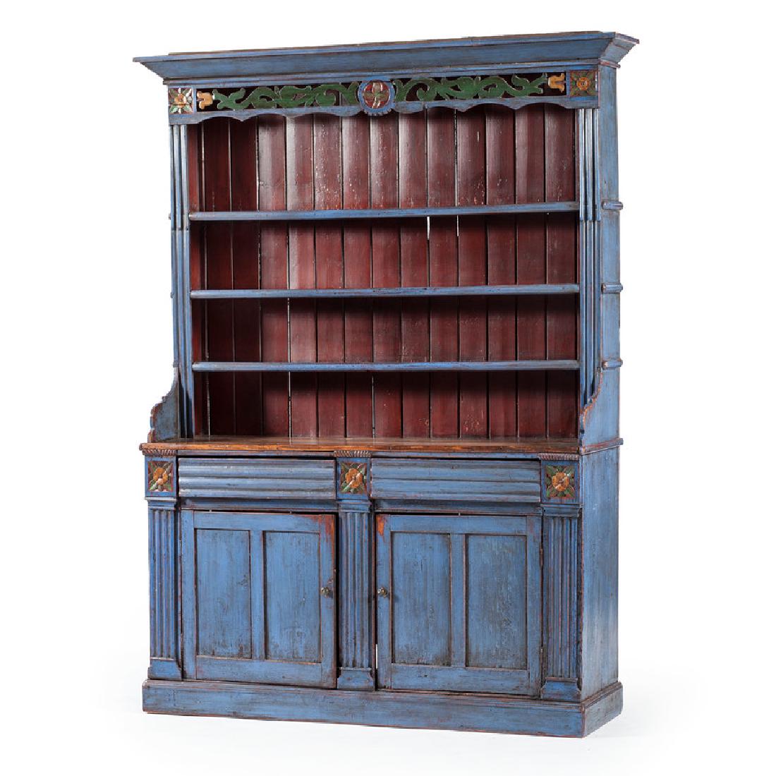 English Painted Pewter Cupboard: English, 19th century. A blue painted pewter cupboard in pine, having a molded cornice, above an open carved frieze flanked by carved rosettes and open three shelf interior, the lower case having two 