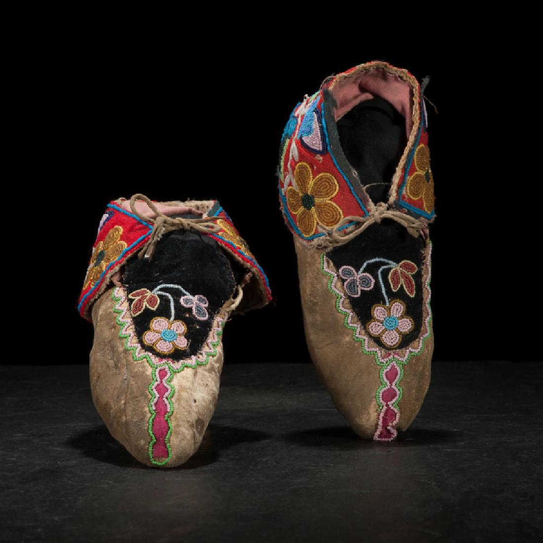 Anishinaabe Beaded Hide Moccasins: thread-sewn, with colorful designs executed using red wool, black velveteen, pink sateen, and assorted bead colors; flowers surround cuffs and are situated on vamps; lined with pink cotton, length 9.5