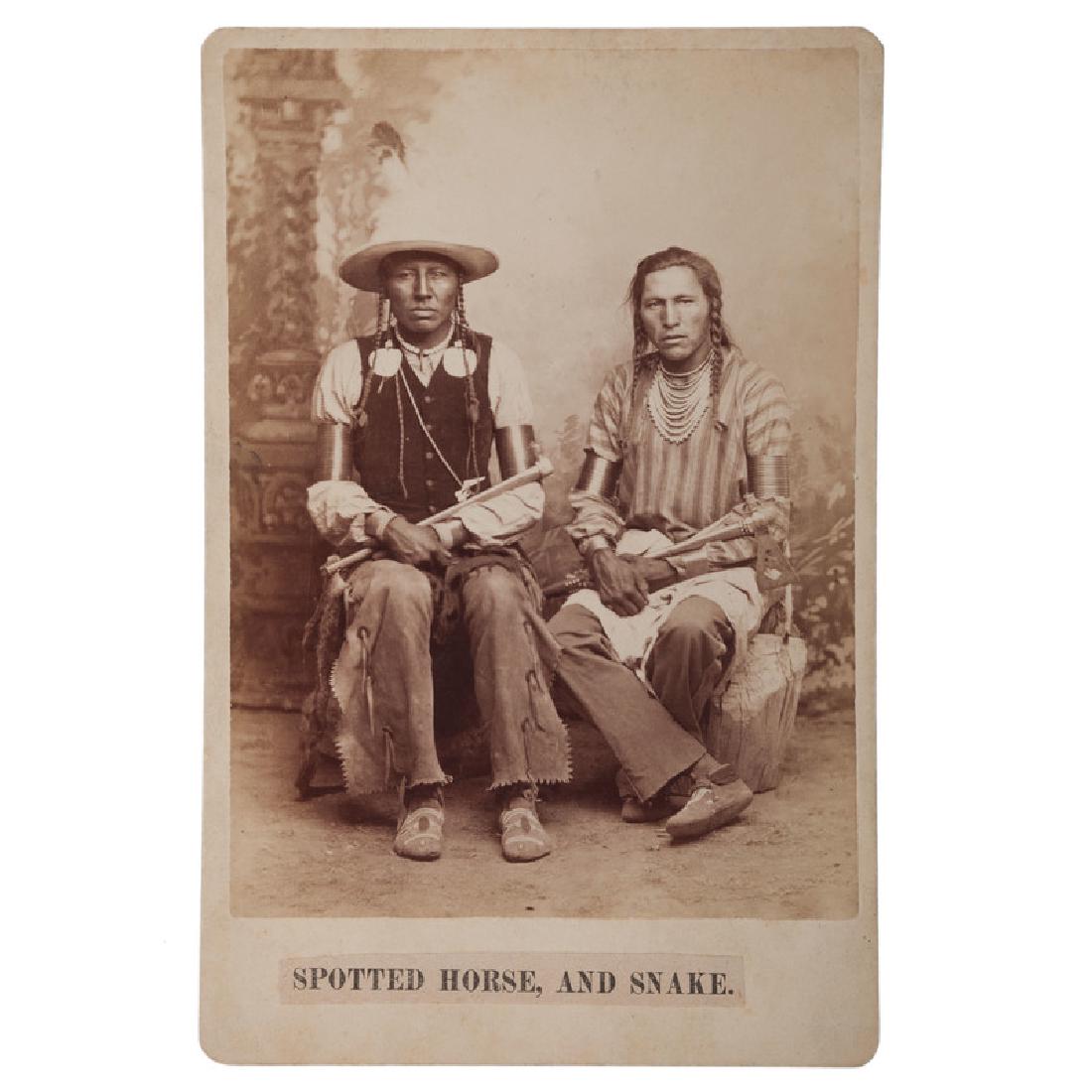 Two Cabinet Cards of Crow Indians by D.F. Barry: Lot of 2 cabinet cards by D.F. Barry, each with printed, applied paper caption, the first from Bismarck, D.T., showing "Spotted Horse, and Snake." Both men wear metal arm bands and hold tomahawks; the