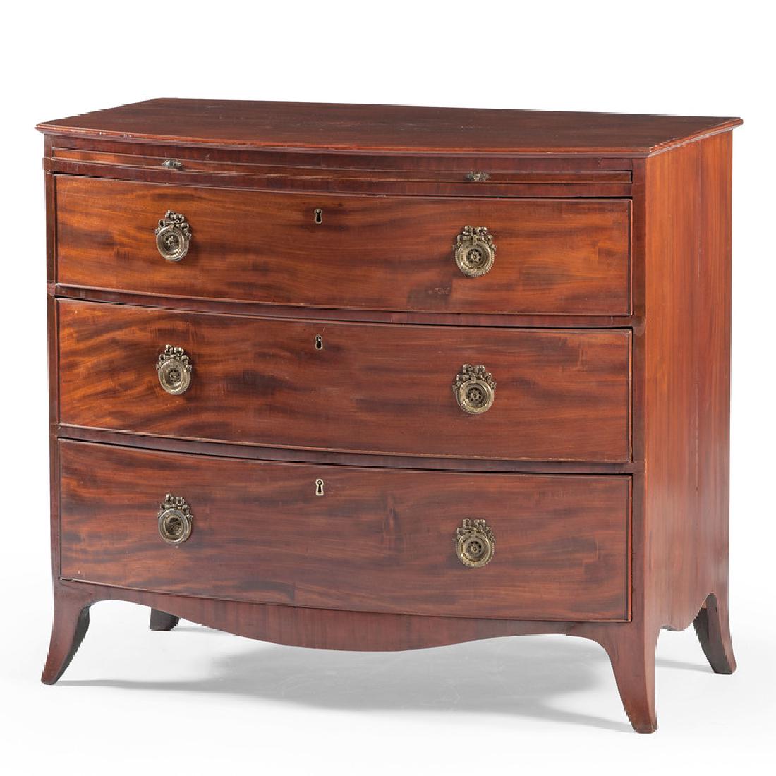 English Hepplewhite Bowfront Chest: English, 19th century. A Hepplewhite bowfront chest with flame mahogany, having a shaped surface over a pull-out writing surface, three graduated and cockbeaded drawers with brass pulls, shaped apron 
