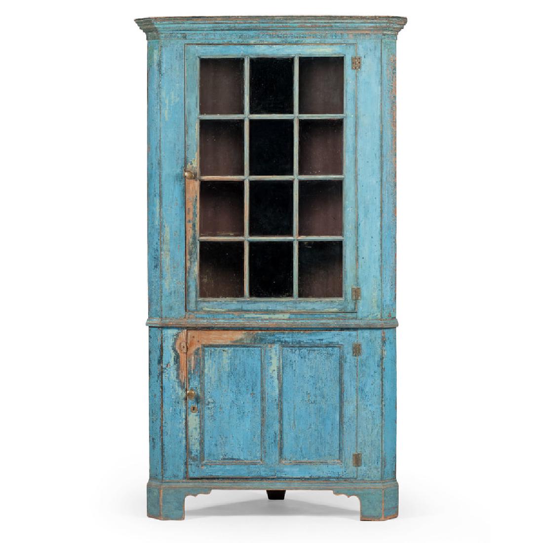 Southern Blue Painted Corner Cupboard: American, first quarter 19th century. A Southern two piece blue painted corner cupboard in yellow pine, the upper section having a stepped molded cornice with canted corners over a single butterfly hi