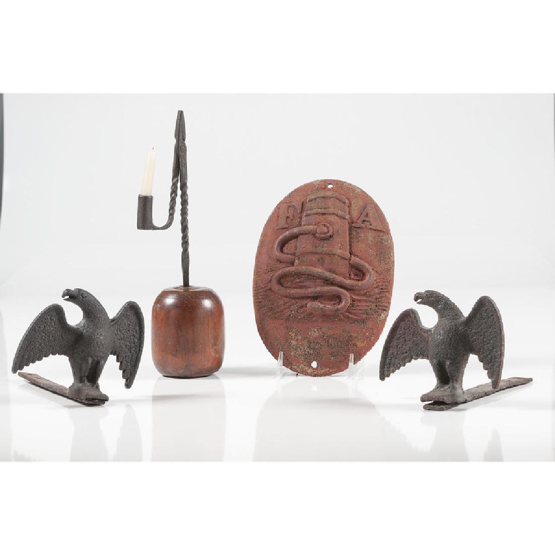 Cast Iron Eagle Snow Guards, Fire Mark, and Candle: American. A collection of cast iron items including a pair of eagle snow guards, a red-painted fire plaque, and a candle holder on a wooden base; plaque lg. 11 in., candle holder ht. 14, snow guards h