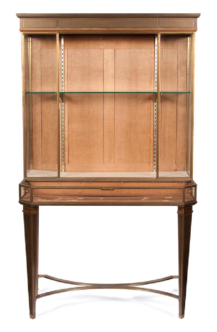 Escalier de Cristal Bronze Vitrine: French, early 20th century. An Escalier de Cristal step-back vitrine in bronze, the upper case illuminated, the lower with lift top, all rising on straight legs connected by curved X-shaped stret