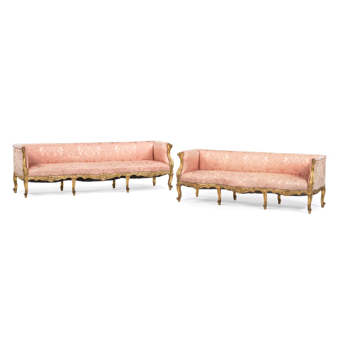 Louis XVI-Style Canapés: French, 19th century (Napoleon III). Two Louis XVI-style giltwood sofas, having straight crest rails with upholstered backs and seats, padded arms with carved swirl terminals, upholstered seats above 