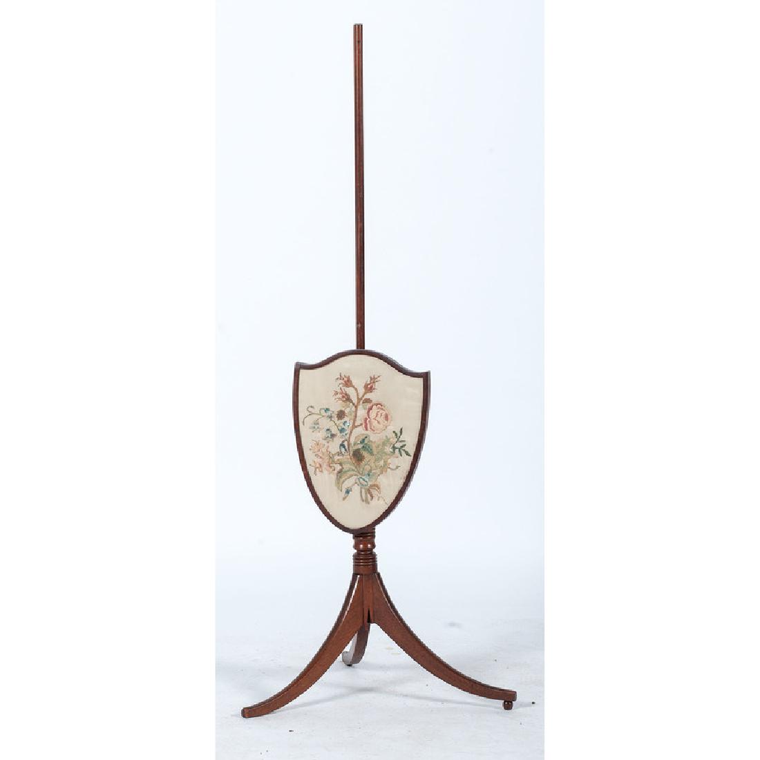 American Pole Screen: American, 19th century. A Hepplewhite fire screen on stand, having a shield shaped screen with floral needlework, rising on tripod saber legs; ht. 54, wd. 22, dp. 21 in. Provenance: Property Sold to b