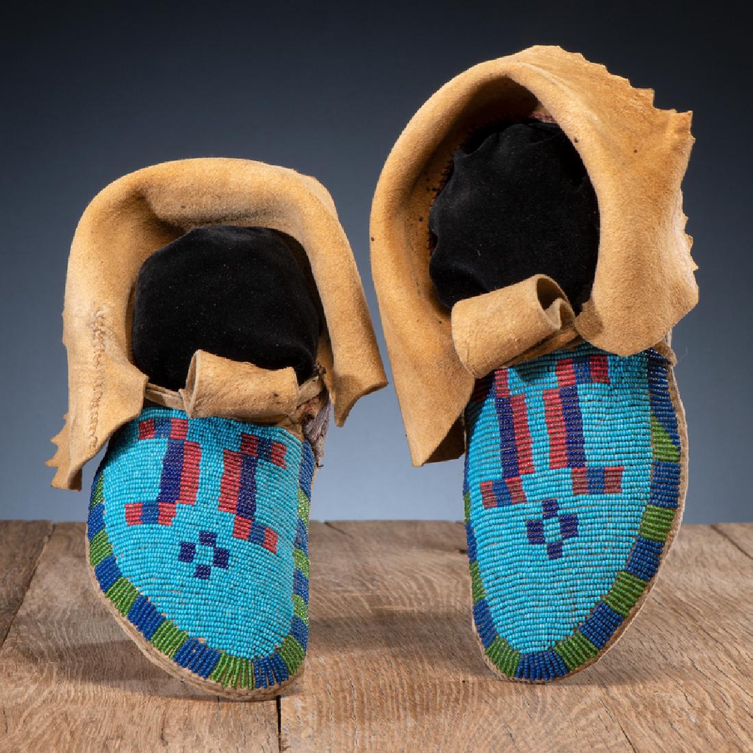 Blackfeet Beaded Hide Soft-Soled Moccasins: thread and sinew-sewn with vamps beaded in colors of light blue, dark blue, red white-heart, rose, and translucent green; folded cuffs have pinked edge, length 10 in. fourth quarter 19th century