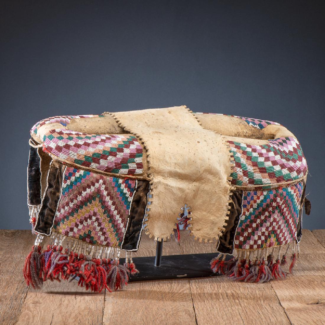 Plains Cree Beaded Hide Pad Saddle: thread and sinew-sewn softly tanned hide; checkered design beaded using colors of translucent green, assorted pinks, white, rose, and light and medium blue; panels further embellished with clear baske