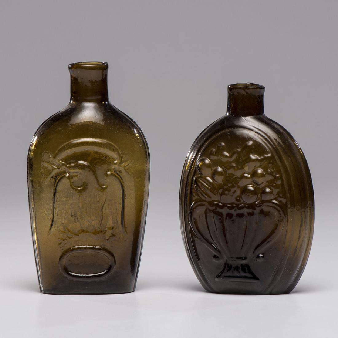 New England Pattern Molded Flasks: American, 19th century. Two pattern molded olive glass flasks, one with an eagle to both sides and the other with two cornucopia variations; larger ht. 6 in.