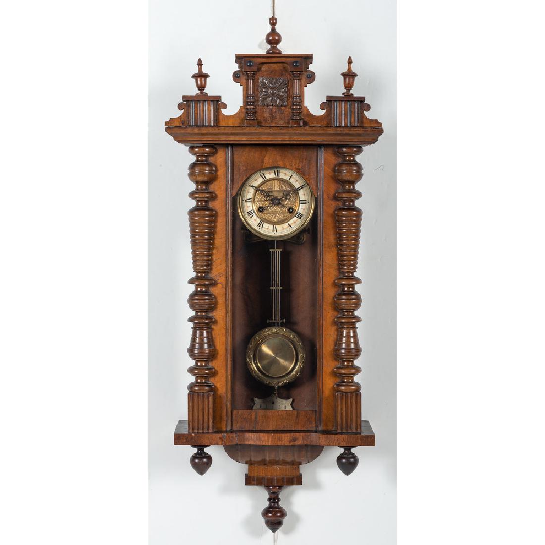 Victorian Wall Clock: American 19th century. A Victorian hanging wall clock in mahogany with pine secondary, having a stepped and molded removable crest with carved panels and turned finials, the open pane pendulum door wi