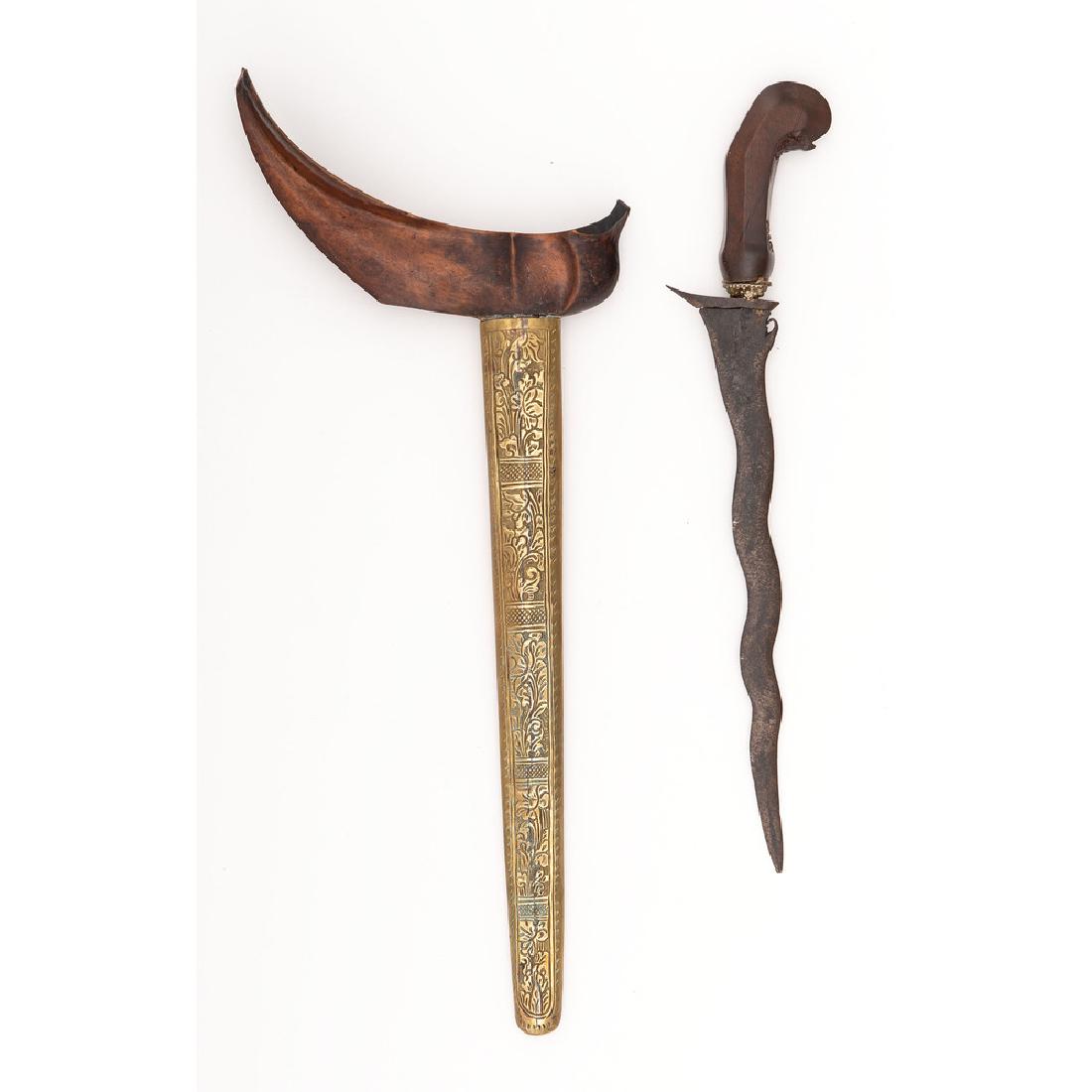 Indonesian Keris: 11" double edged blade featuring seven luk (waves) and no visible pamor (pattern). Carved wood grip. Wood scabbard with brass wrap showing floral motifs. Provenance: Purchased by consignor