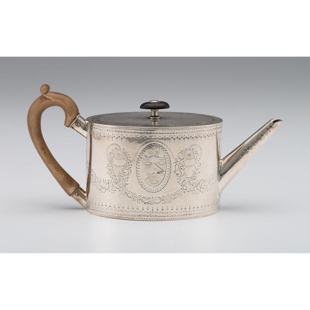 George III Sterling Teapot with Engraved Decoration: English (London), ca 1783. A sterling silver oval teapot with fine bright cut decoration throughout including an armorial cartouche, with wooden handle and finial. With full hallmarks to underside inc