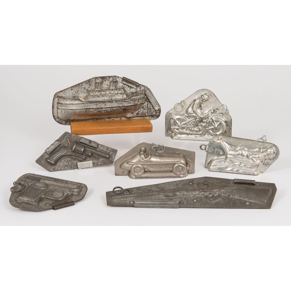 Tin Chocolate Molds: Tin Chocolate Molds 20th century. A group of seven tin chocolate molds. Shapes include three firearms, a sledding child, a man on a motorcycle, a race car, and a steamship with stand; largest lg. 12.5